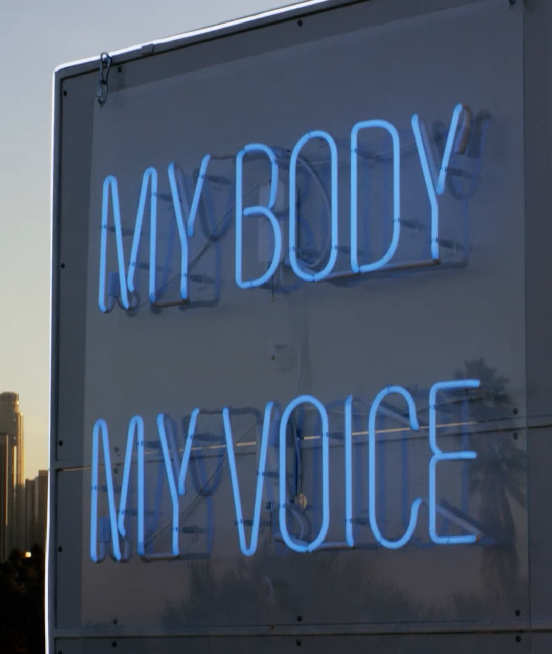 Image of the VoiceBox, in the park, with a glowing neon sign which states, my body my voice.